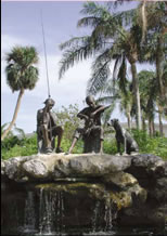 Statue figures on stone waterfall of two people fishing and dog sitting nearby 